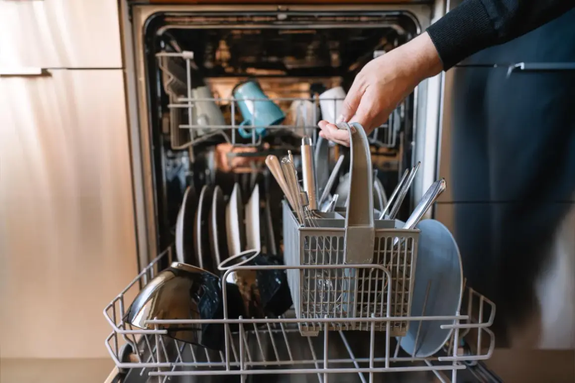 Ręka wkłada koszyk ze sztućcami do zmywarki. To oznacza, że naczynia są "dishwasher safe", czyli można je myć w zmywarce.