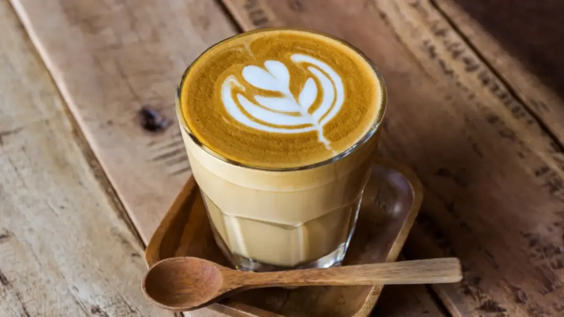 En vacker caffe latte med latte art på ett träbord. En träsked ligger bredvid.