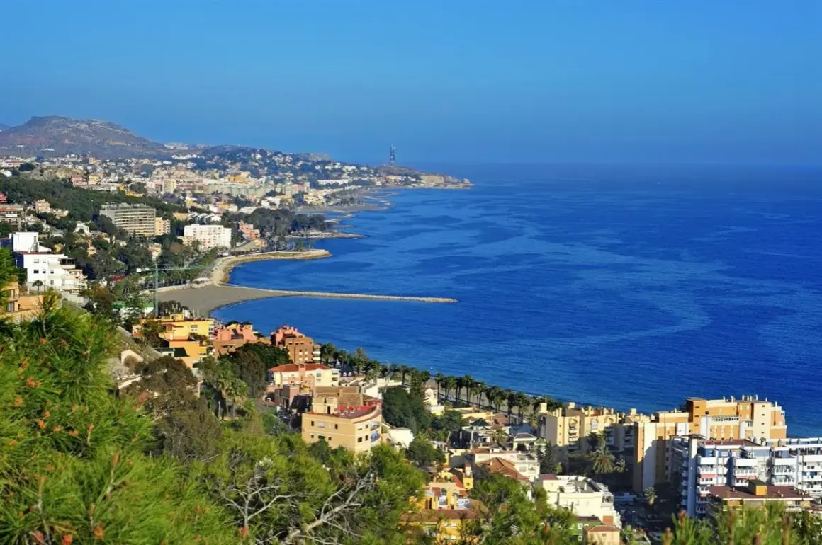 Widok na malaga plaże i miasto z zielonymi wzgórzami w tle. Błękitne morze lśni w słońcu.