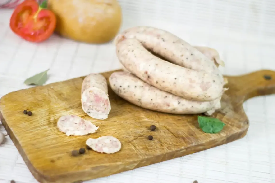 Gotowy przepis na białą kiełbasę na 5 kg. Na desce leżą świeże kiełbaski, przyprawy i pomidor.