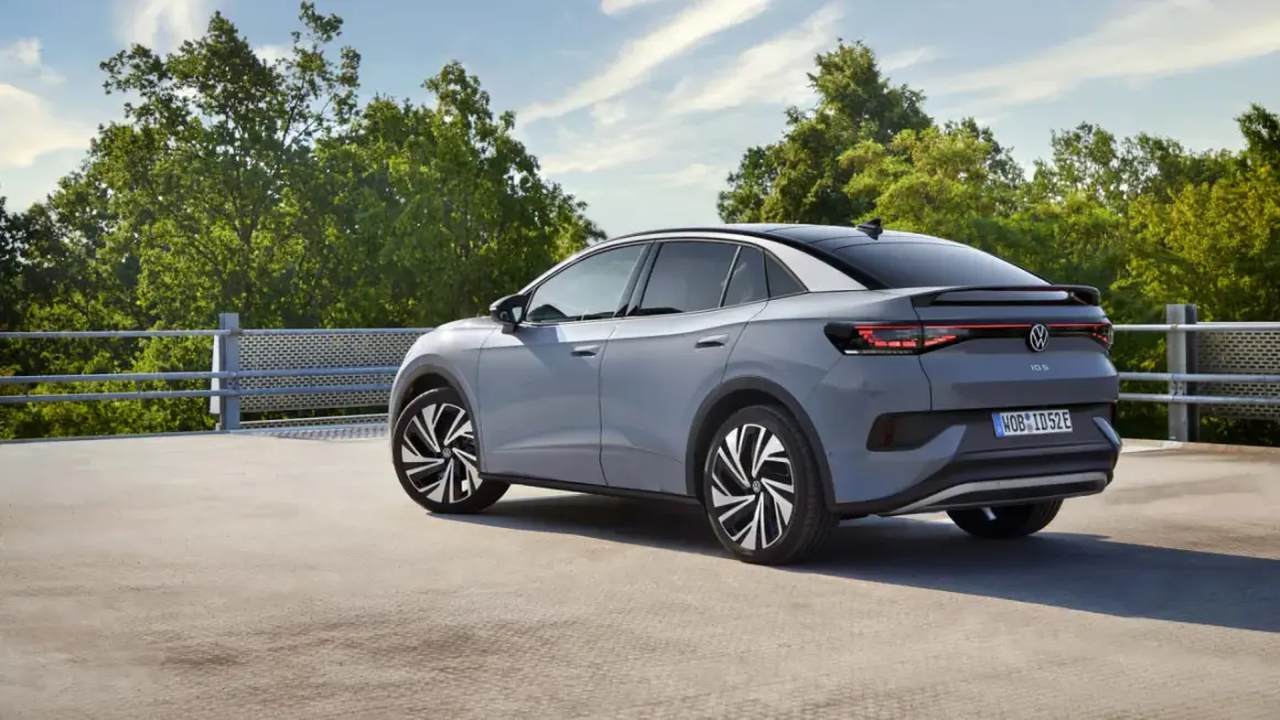 El Volkswagen ID.5 gris, con su diseño deportivo, se detiene en un día soleado, rodeado de árboles verdes y un cielo azul.