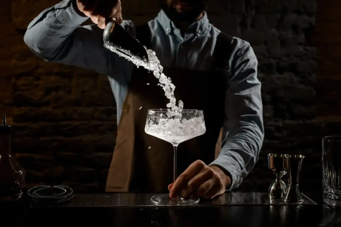 Barman aggiunge ghiaccio tritato in un calice. La corretta temperatura frigo bar bevande è fondamentale per un cocktail perfetto.