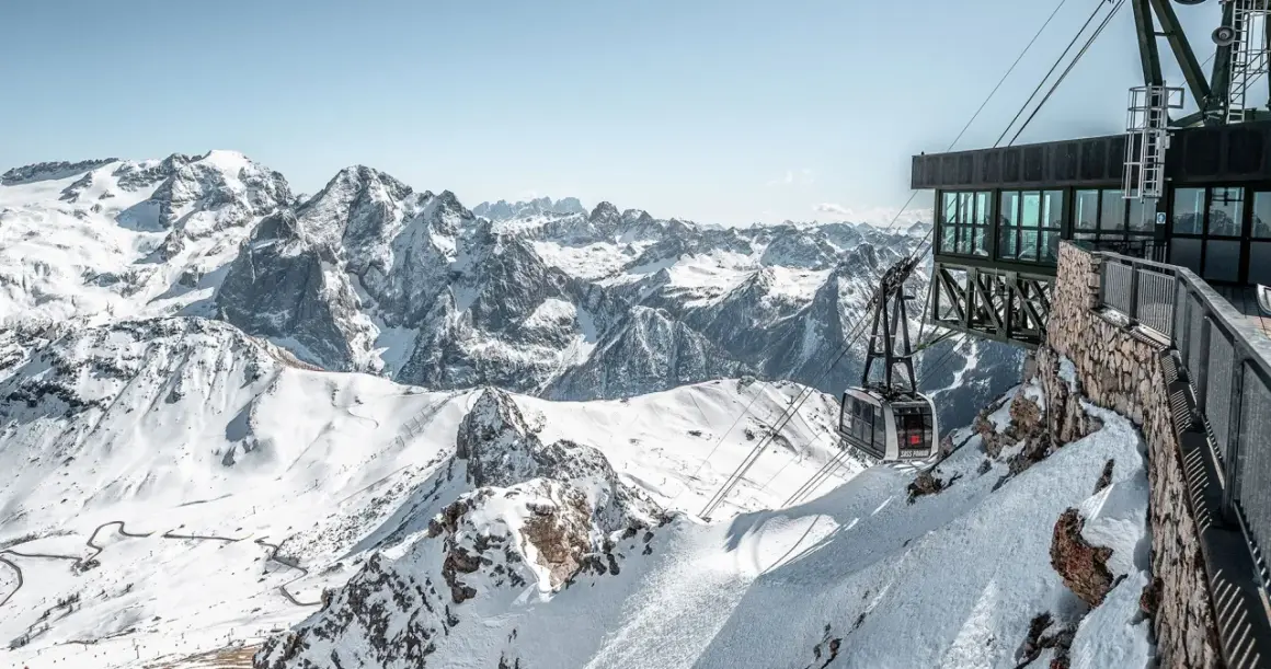 Panoramica mozzafiato dal belvedere di Canazei: una funivia scende tra le cime innevate delle Dolomiti.