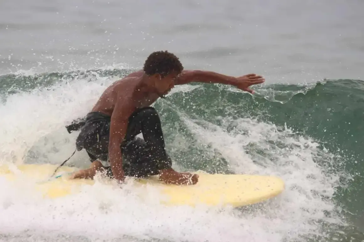 Un jeune homme surfe sur une vague à Tamraght, éclaboussant d'eau.