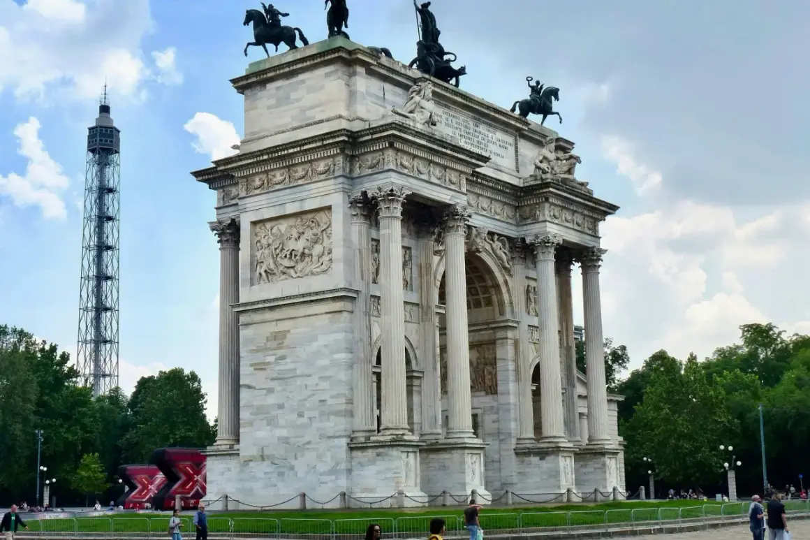 Arco di Pace a Milano, con la torre bianca sullo sfondo e un cielo nuvoloso.