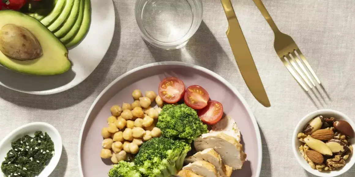 Assiette de poulet, brocolis, pois chiches et tomates, avec avocat et noix. Un repas équilibré pour un rééquilibrage alimentaire réussi.