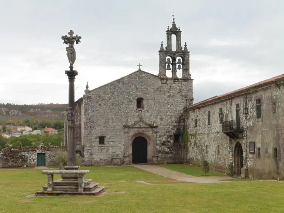 El monasterio de Aciveiro, con su iglesia de piedra y campanario, se alza majestuoso. Un cruceiro antiguo preside el patio.