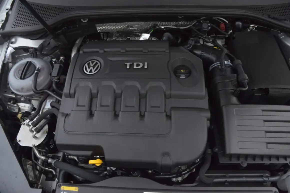 Silnik 2.0 TDI 190 KM. Widok na pokrywę silnika z logo VW i napisem TDI. W tle zbiornik płynu chłodniczego.