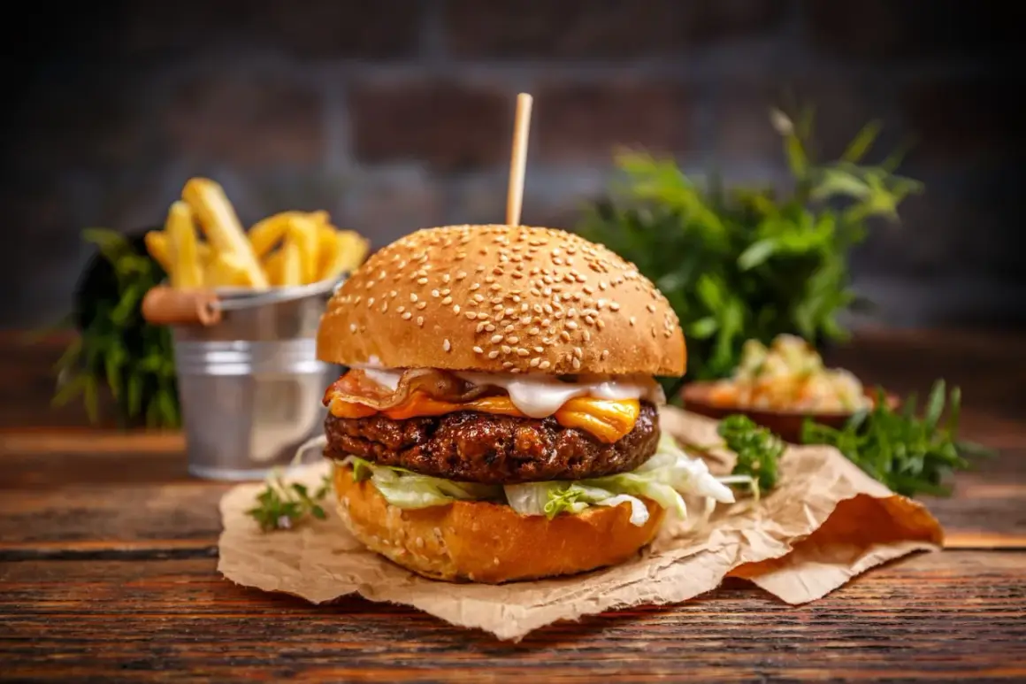 Pyszny burger z bekonem i serem, idealny na dzień burgera. Obok frytki i surówka.