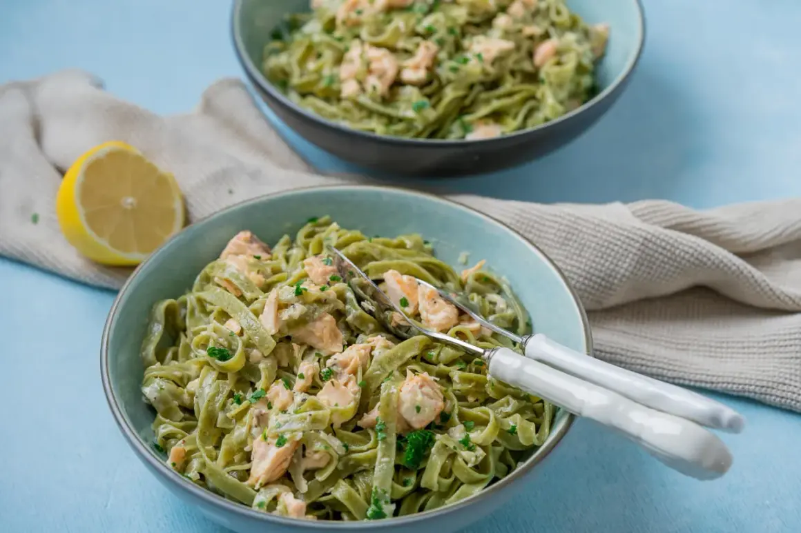 Zwei Schüsseln cremiger Tagliatelle al salmone, garniert mit Petersilie, daneben eine Zitronenhälfte und ein Küchentuch.