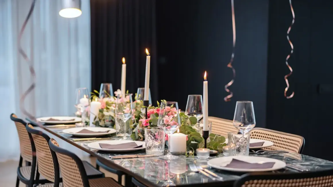 Tavola apparecchiata con candele, fiori rosa e bicchieri per un elegante servizio alla francese.