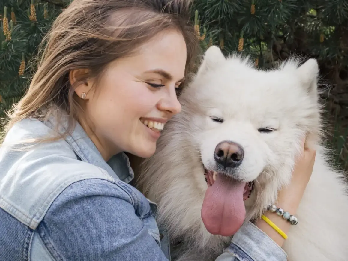 Uśmiechnięta dziewczyna przytula swojego białego psa. To prawdziwy psi tłumacz, który rozumie każde jej słowo.