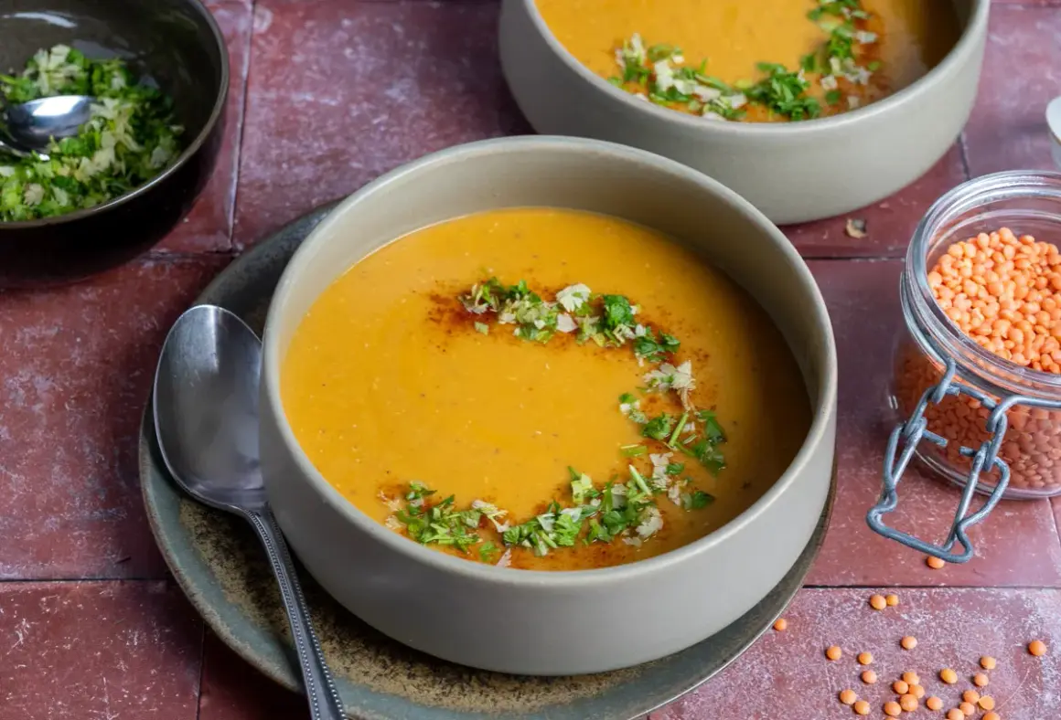 Herzhafte mercimek corbasi, eine cremige Linsensuppe, garniert mit frischen Kräutern und Gewürzen. Daneben eine Schale mit roten Linsen.