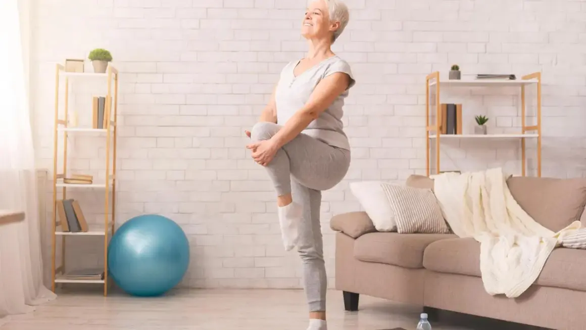 Une femme âgée sourit en faisant un exercice d'équilibre, idéal pour une fiche technique gym douce pour personne âgée.