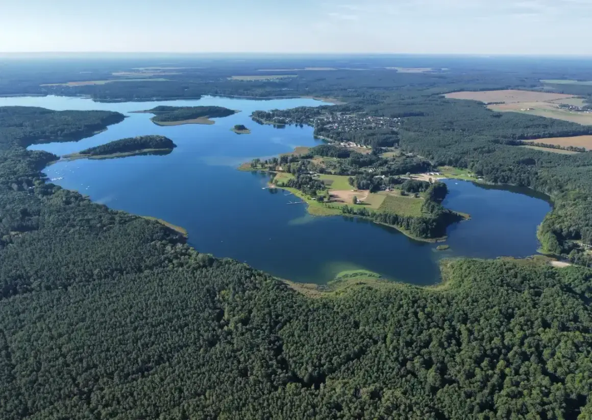 Malownicze jezioro Niesłysz otoczone lasami, z widocznymi wysepkami i zabudowaniami na brzegu.