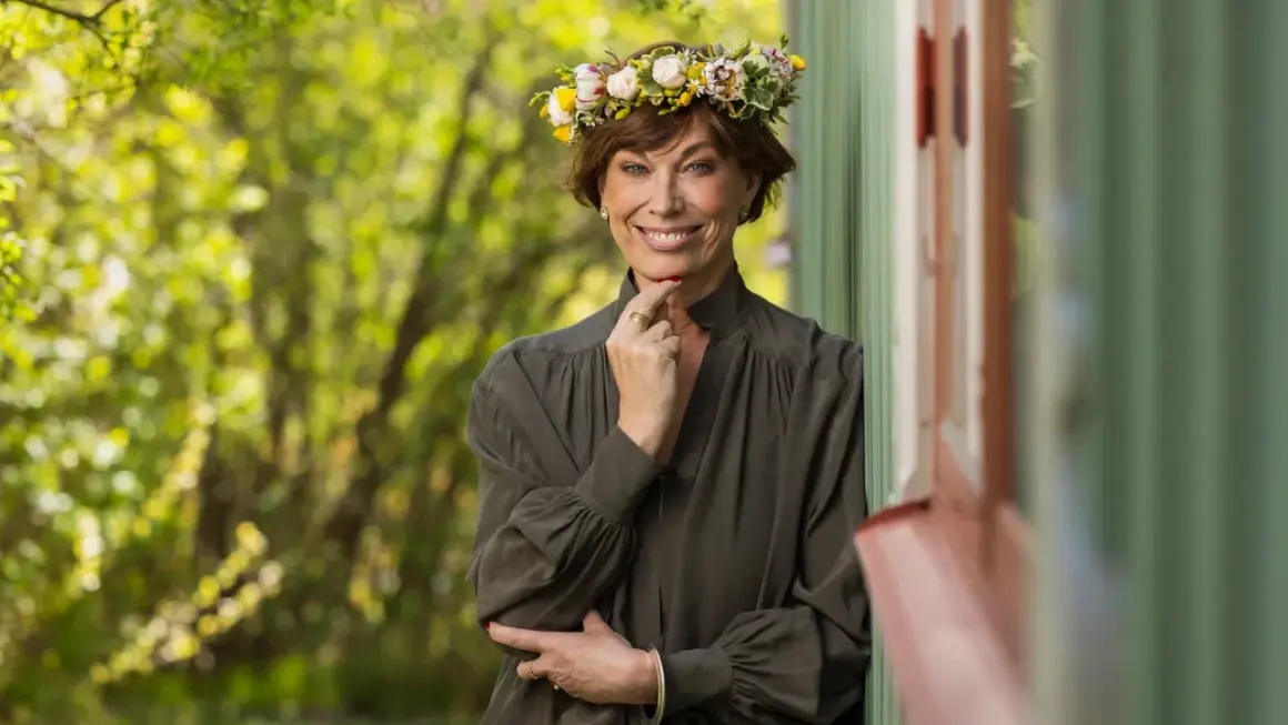 En kvinna med blomsterkrans ler mot kameran. Hon påminner om en sommarbild av mischa billing familj.