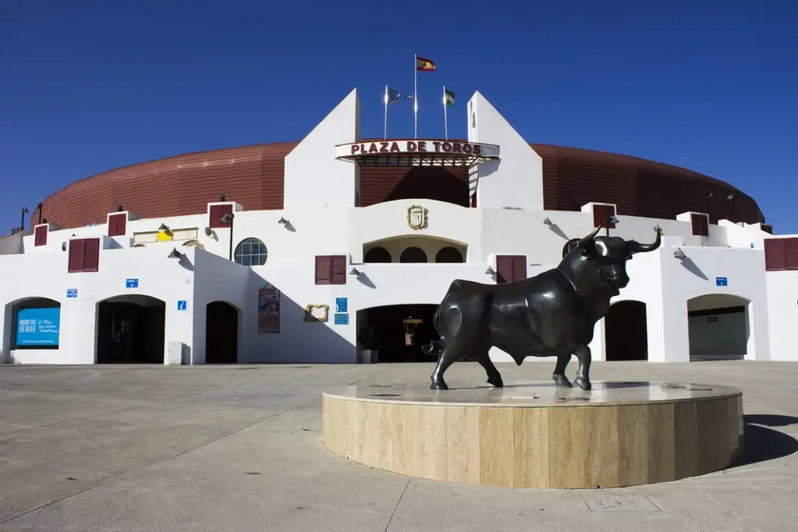 Escultura de toro frente a la Plaza de Toros Roquetas de Mar, bajo un cielo azul intenso.