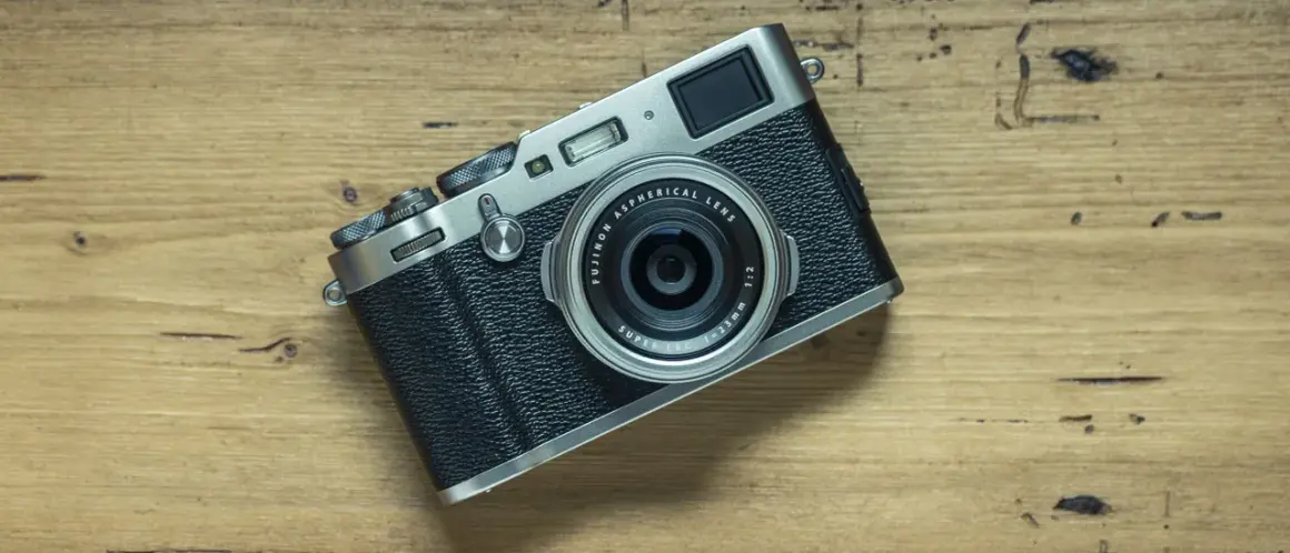 En Fujifilm X100T-kamera ligger på en träyta. Dess retrodesign och fasta objektiv gör den till en favorit för gatufotografering.