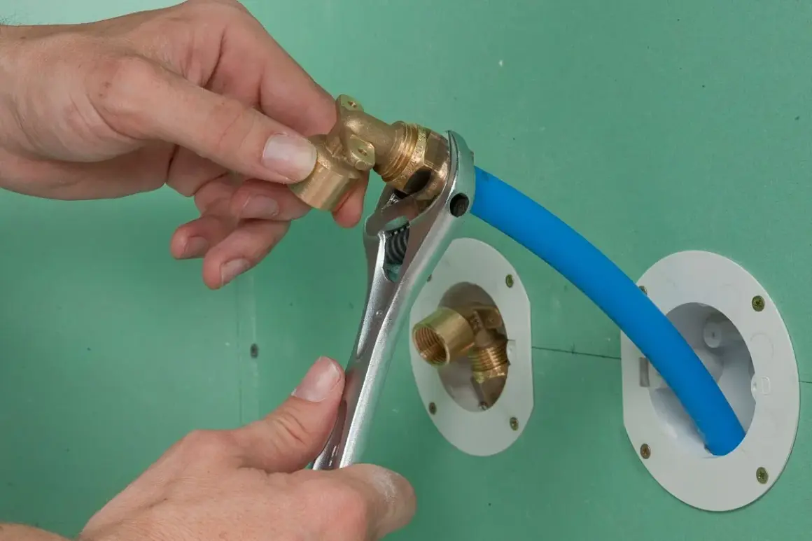 Installation d'un raccord pour l'arrivée d'eau de la douche. Une clé serre un coude en laiton sur un tuyau bleu.