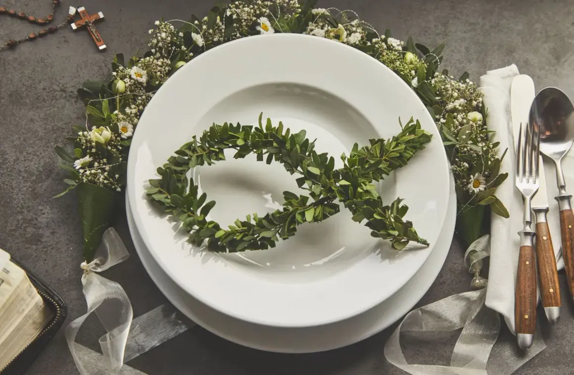 Eleganckie menu na komunię w domu. Na talerzu symbol ryby z gałązek, wokół kwiaty i różaniec.