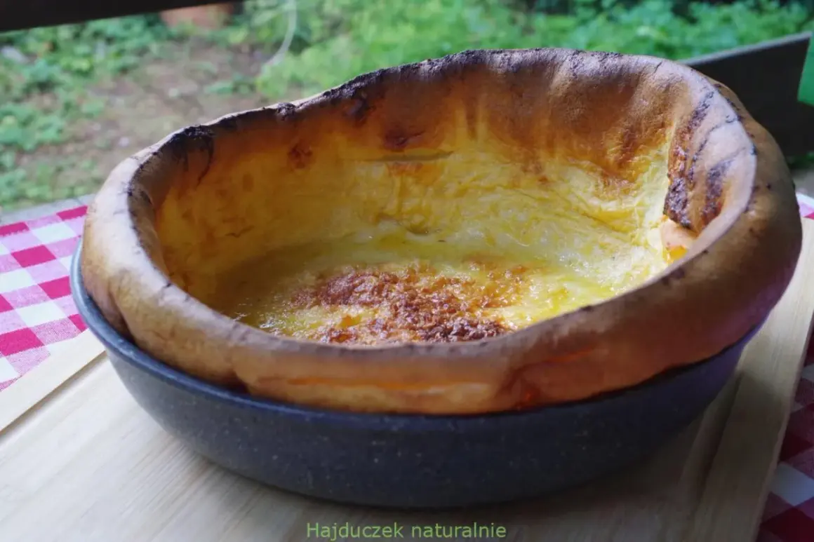 Puszysty, złocisty dutch baby, lekko przypieczony na brzegach, w okrągłej formie.