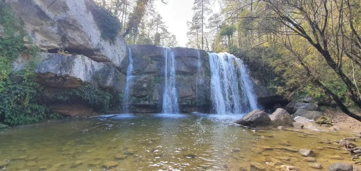 Cascada en la ruta 7 gorgs, con rocas cubiertas de musgo y vegetación, y un río de aguas claras.