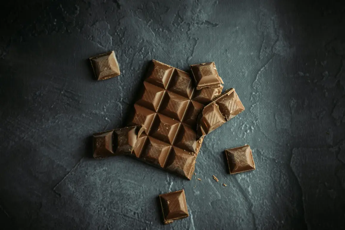 Tableta de chocolate rota y trozos sueltos sobre fondo oscuro. ¡Sí, puedo llevar chocolates en la maleta de mano!