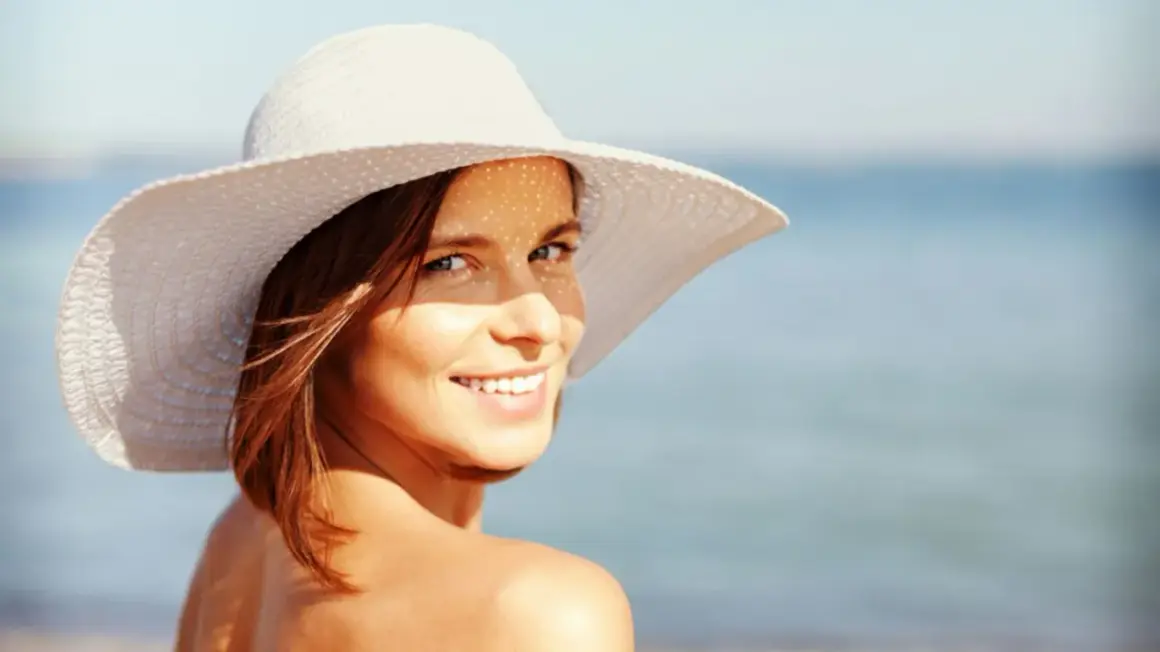 Frau mit Hut am Strand, genießt die Sonne mit Sonnencreme LSF 50 Gesicht.