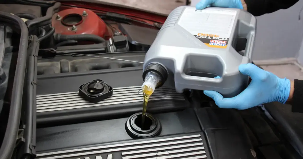 Ręce w niebieskich rękawiczkach wlewają olej silnikowy Liqui Moly do silnika. Czy można mieszać oleje silnikowe? To pytanie nurtuje wielu kierowców.