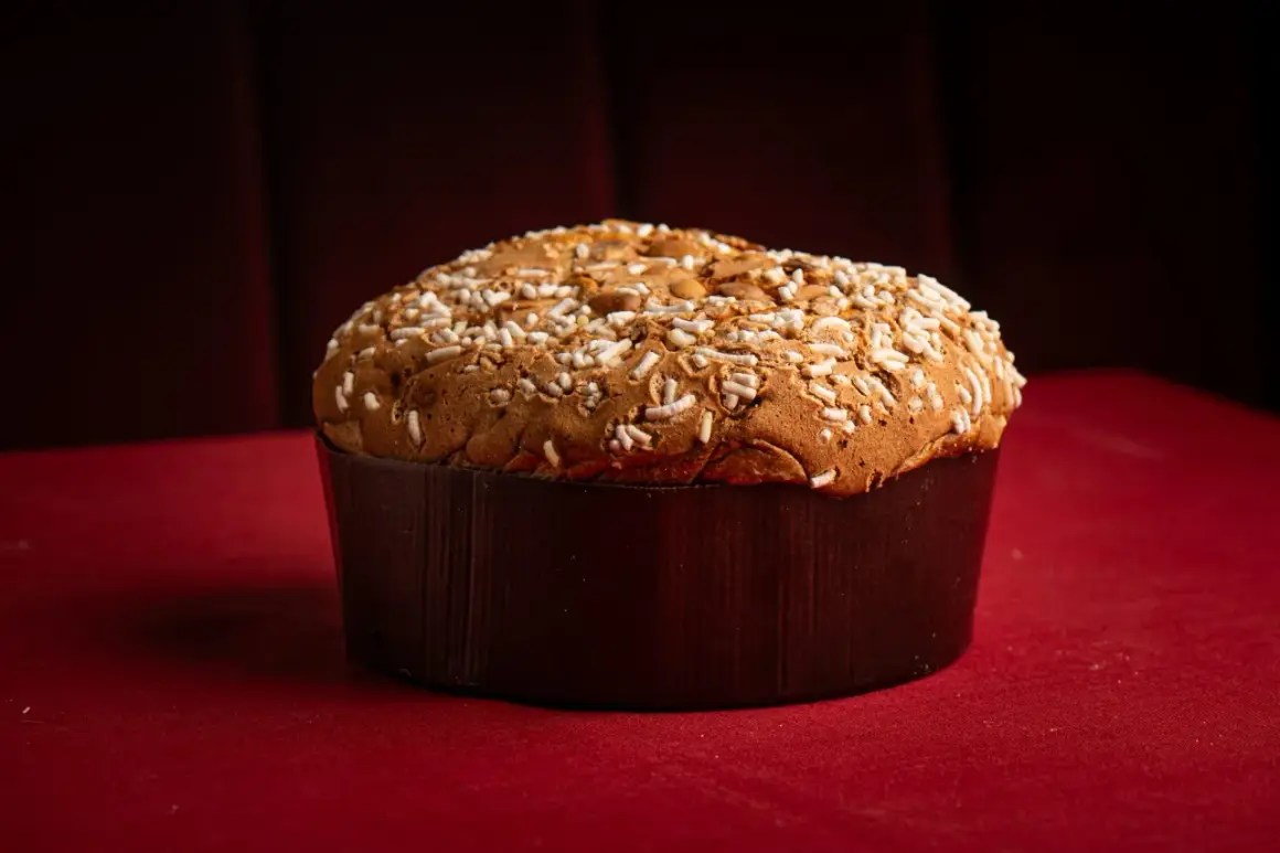 Un panettone tradicional, uno de los tipos de panettone, cubierto con azúcar perlado y almendras, sobre un mantel rojo.