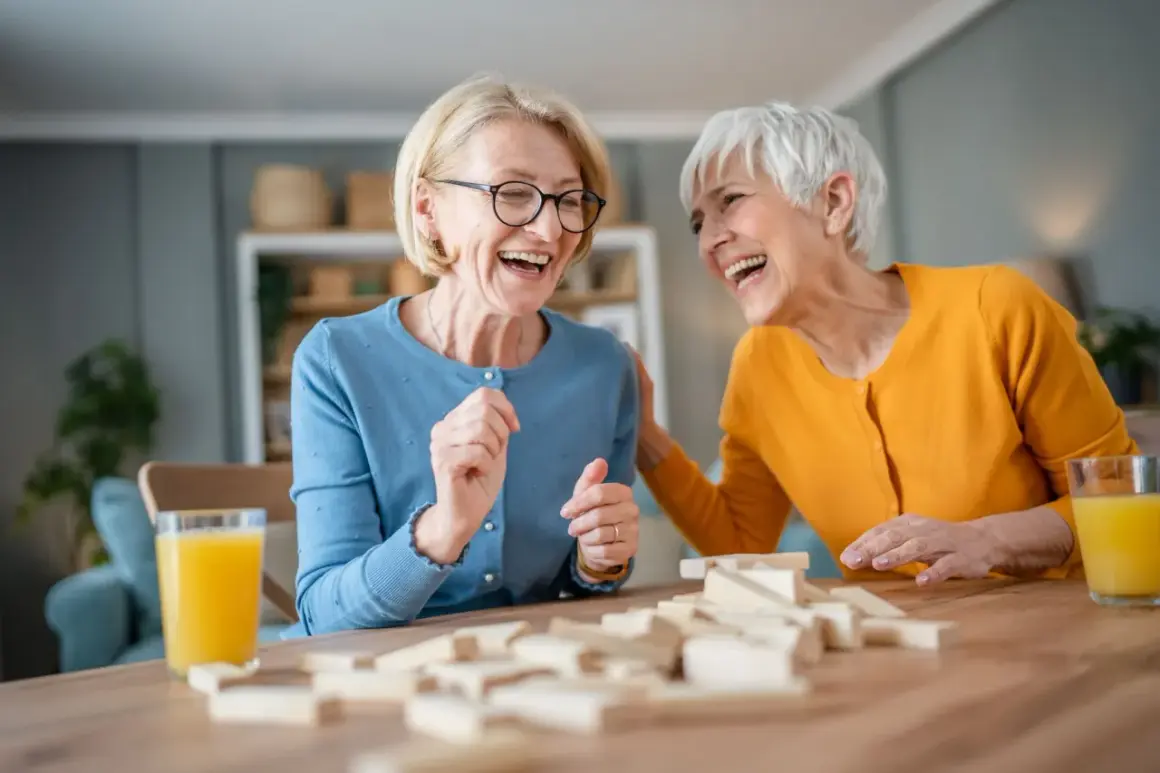 Deux femmes âgées rient en jouant au Jenga, une activité maison de retraite pleine de joie et de complicité.