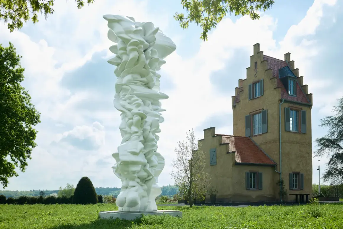 Weiße, organische Skulptur vor einem gelben Gebäude im Freien.