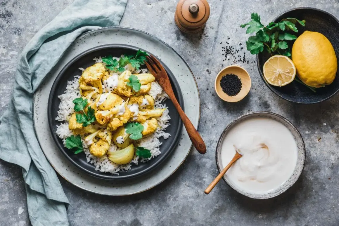 Würziges Karfiol-Rezept mit Reis, garniert mit Koriander und Tahini-Sauce. Dazu Zitrone und schwarzer Sesam.