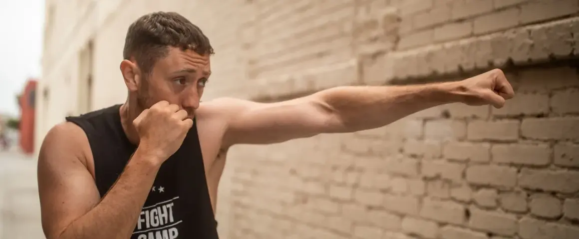 Man practicing boxing, demonstrating how to increase punching power at home with a focused stance against a brick wall.