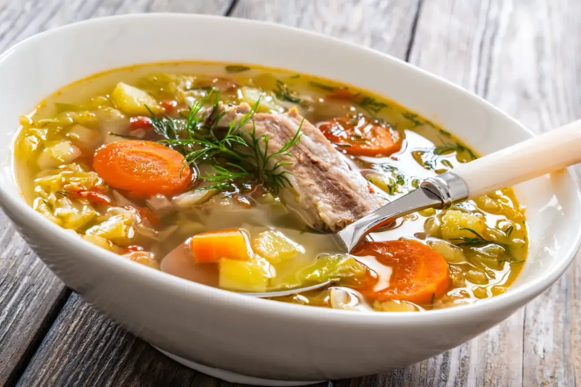 Aromaticzna zupa na żeberkach z warzywami i koperkiem, podana w białej misce na drewnianym stole.