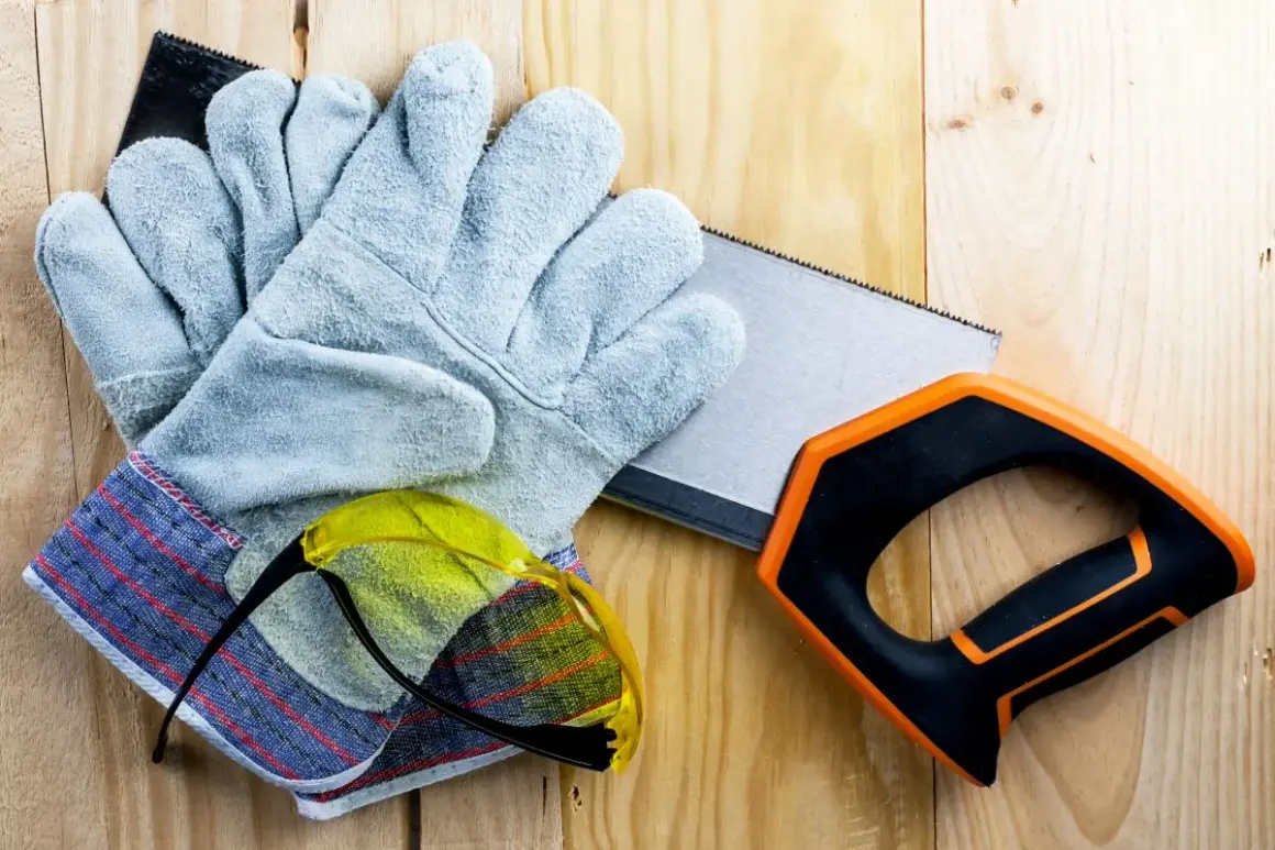 Guantes anticorte niveles, gafas de seguridad y sierra de mano sobre madera.