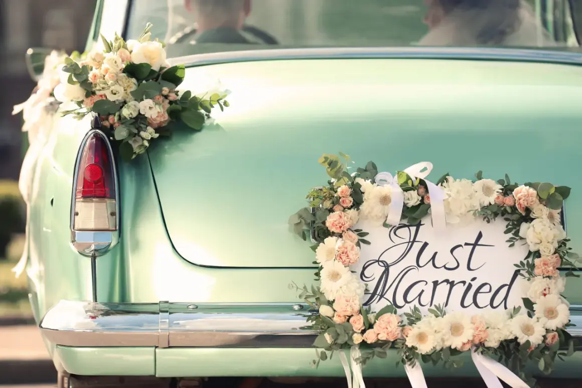 Hochzeitsauto mit Blumen geschmückt, "Just Married" Schild. Ein besonderer Urlaub nach der Hochzeit, vielleicht mit einem Kind auf dem Weg.