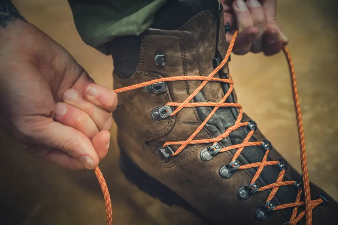 Hände binden orange Schnürsenkel an braunen Wanderschuhen. Bereit für das nächste Abenteuer.
