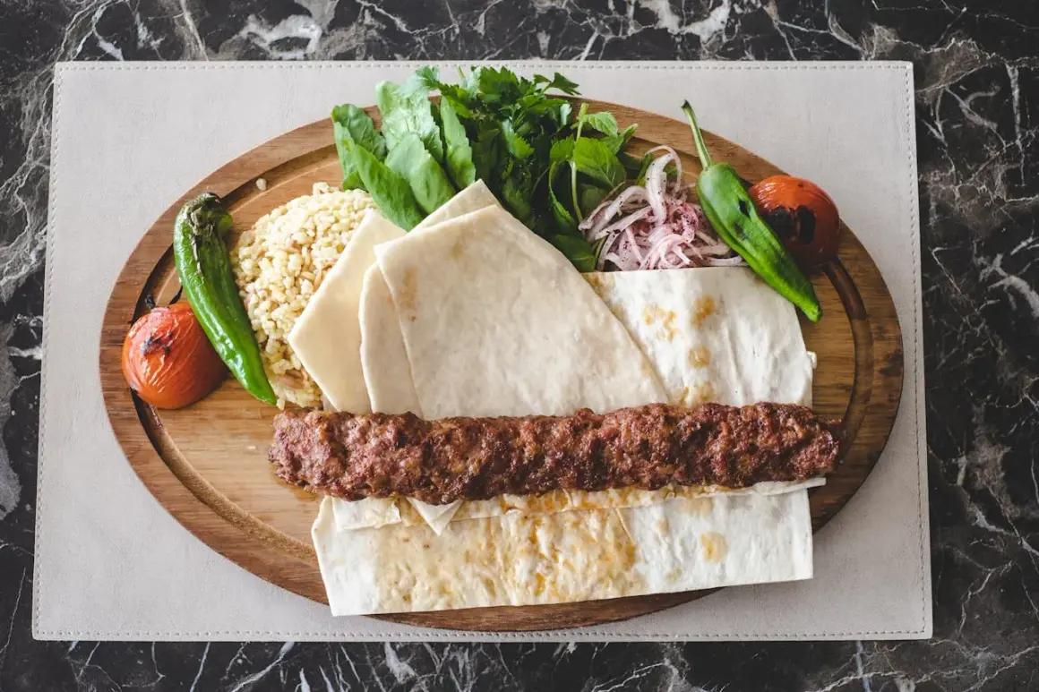 Pyszny kebab na szpadzie z ryżem, pieczonymi warzywami, świeżymi ziołami i cienkim pieczywem.