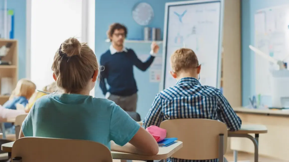 Nauczyciel tłumaczy coś dzieciom w klasie. Zastanawiasz się, ile zarabia nauczyciel klas 1-3?