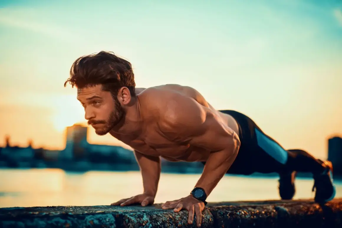 Mężczyzna wykonuje pompki na biceps przy zachodzie słońca nad wodą.