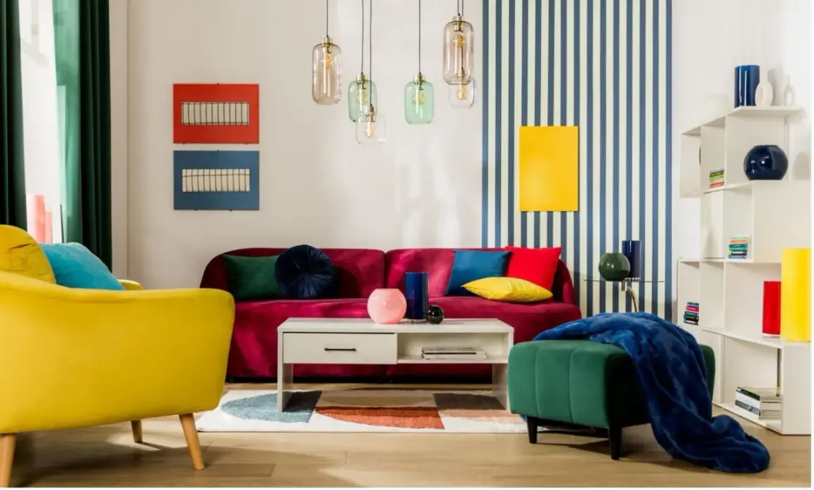 Salon w stylu memphis: żółty fotel, bordowa kanapa, kolorowe poduszki, geometryczny dywan i lampy.