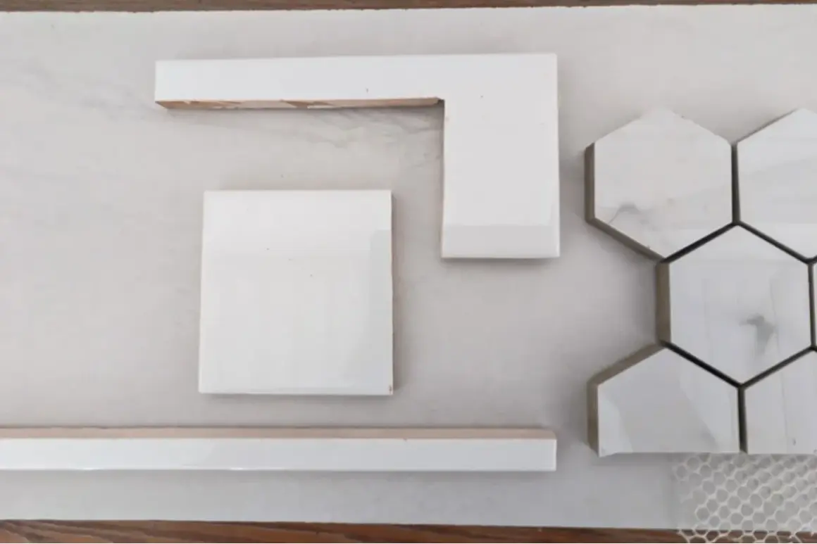 White wall tiles, including square, L-shaped, and hexagonal pieces, are laid out on a light surface, hinting at how to cut wall tile for a project.