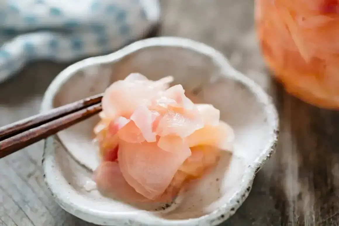 Różowy imbir do sushi, delikatnie podany na talerzyku z pałeczkami. Idealny dodatek do każdego sushi.
