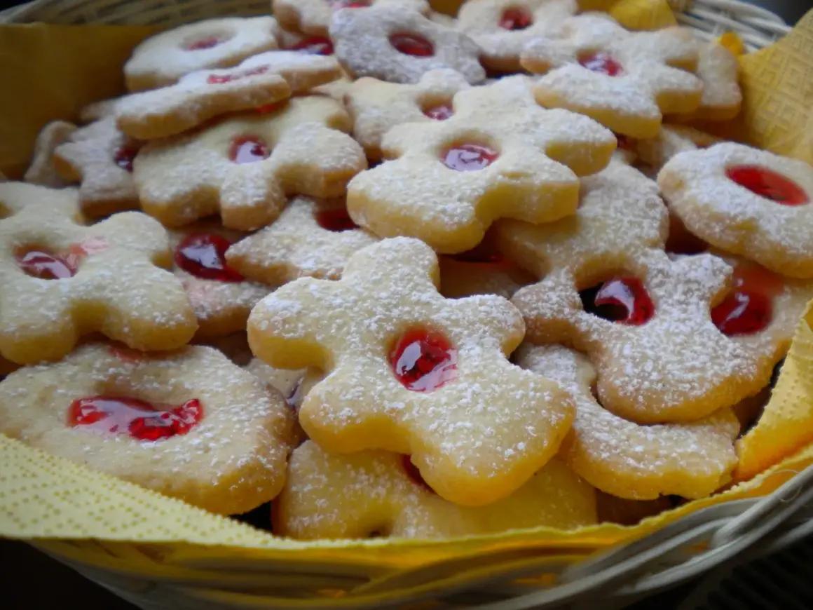 Koszyczek pełen pysznych, kruchych ciasteczek babci, posypanych cukrem pudrem i z czerwonym dżemem w środku.