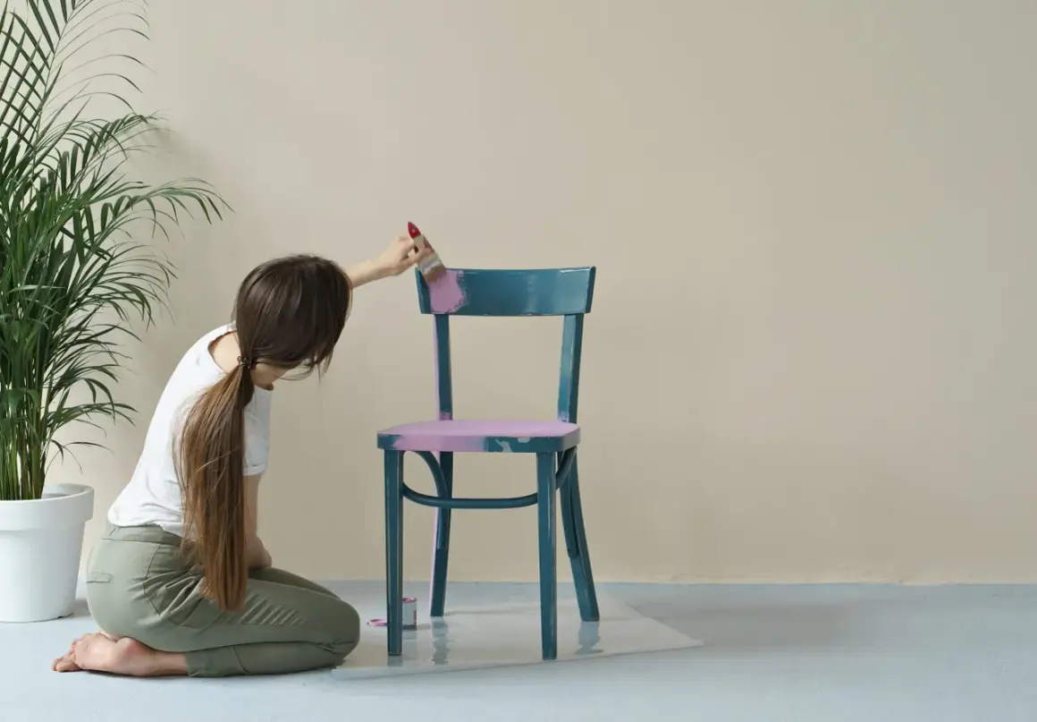 Donna inginoxida una sedia blu con vernice lucida, applicando un colore rosa pastello per opacizzare la finitura.