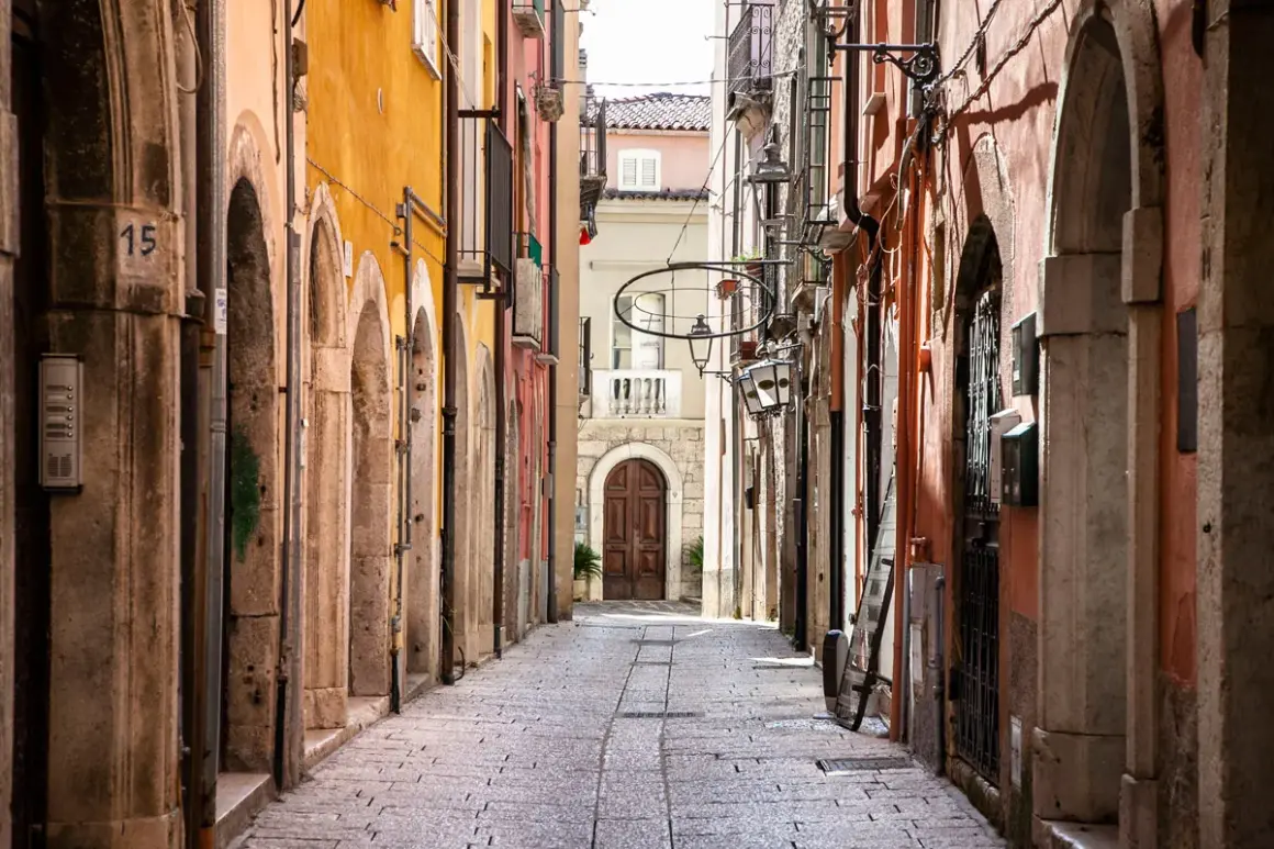 Un vicolo stretto nel chia centro storico, con edifici colorati, archi in pietra e un'antica porta in legno in fondo.