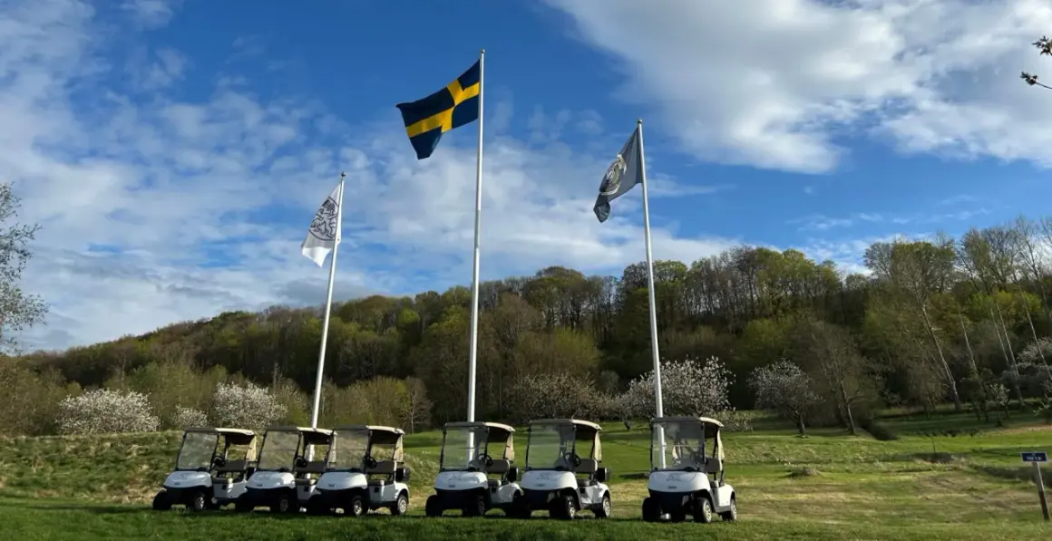 Golfbilar redo för spel vid äppelgården i Båstad. Svenska flaggan vajar stolt i bakgrunden.