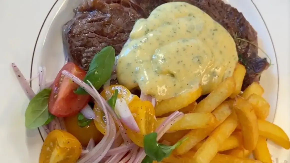 En saftig biff med krämig bearnaisesås, gyllene pommes frites och en fräsch tomatsallad. En klassisk steak frites-upplevelse.