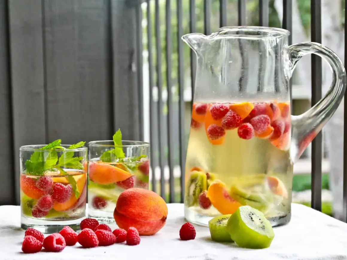 Orzeźwiająca sangria drink z malinami, brzoskwiniami i kiwi w dzbanku i szklankach, ozdobiona miętą.